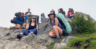 High school students pose on a rock outcropping with program organizer Chloe Moore.
