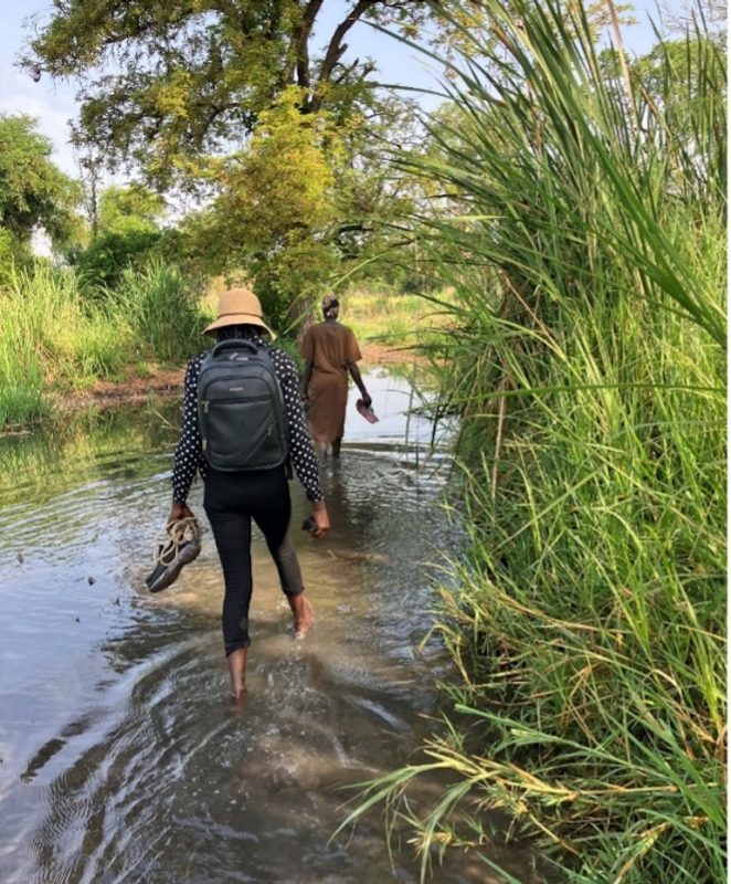 Refugee participant and translator crossing a marsh in search of firewood
