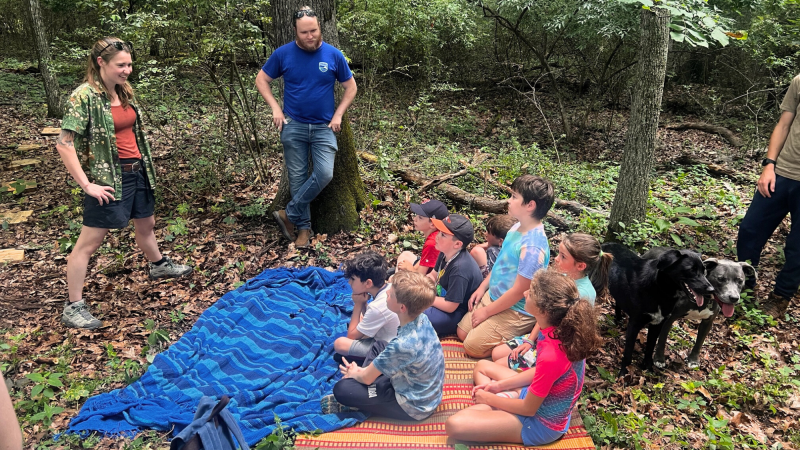 Campers sitting in forested area listening to instructors